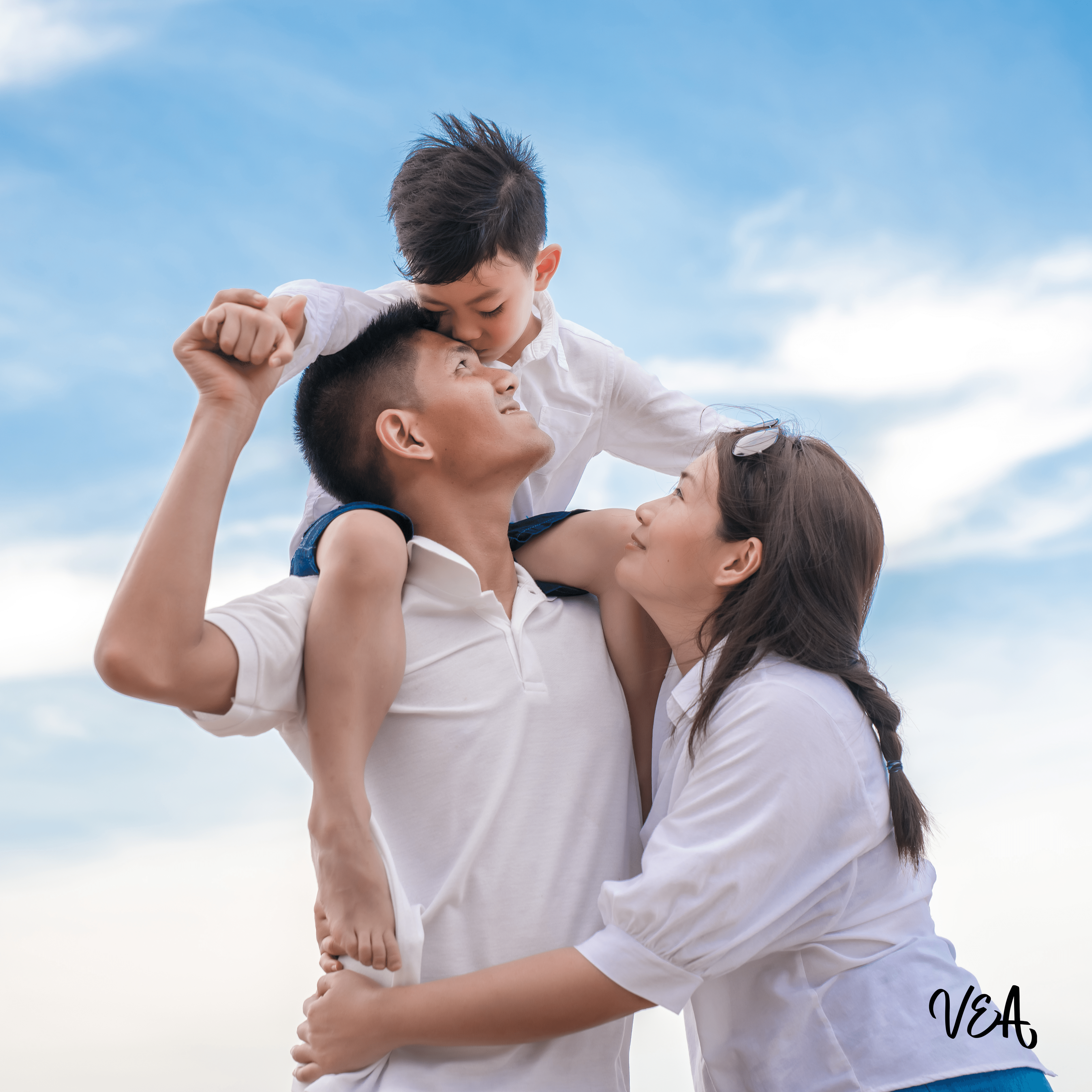 Image d'une famille, couple avec jeune enfant, l'homme porte son enfant sur les épaules, et la femme étreint le monsieur.