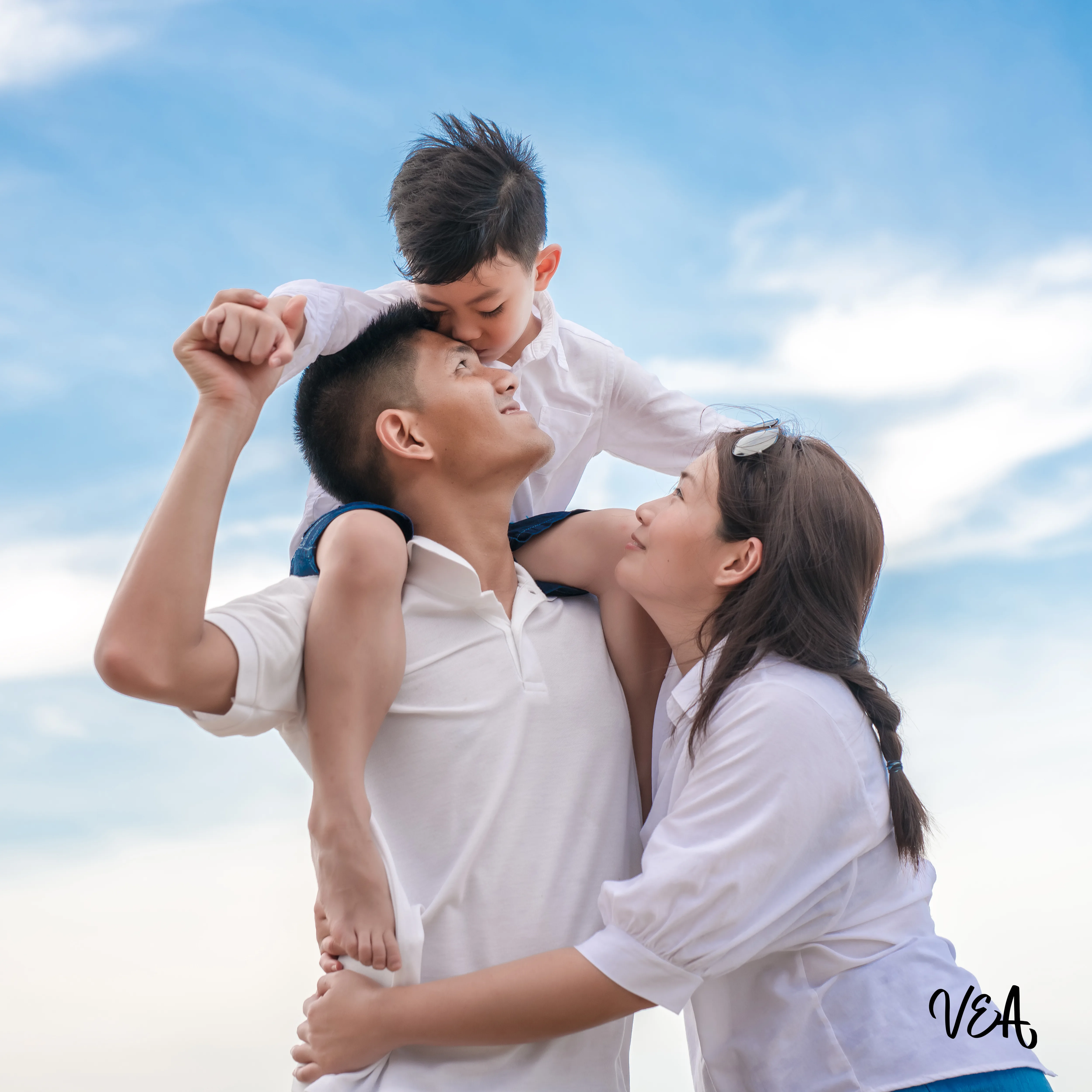 Image d'une famille, couple avec jeune enfant, l'homme porte son enfant sur les épaules, et la femme étreint le monsieur.